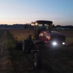 Photo of MacDon swather in a grass seed field with lights on