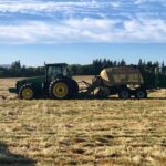 Photo of John Deere tractor pulling Krone baler during straw harvest in grass field