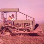 Historical photo of two Berger family members sitting on old John Deere tractor in the field