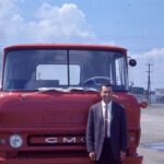 Historical photo of man in front of old red GMC truck