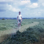 Historical photo of young man standing in field during hay harvest